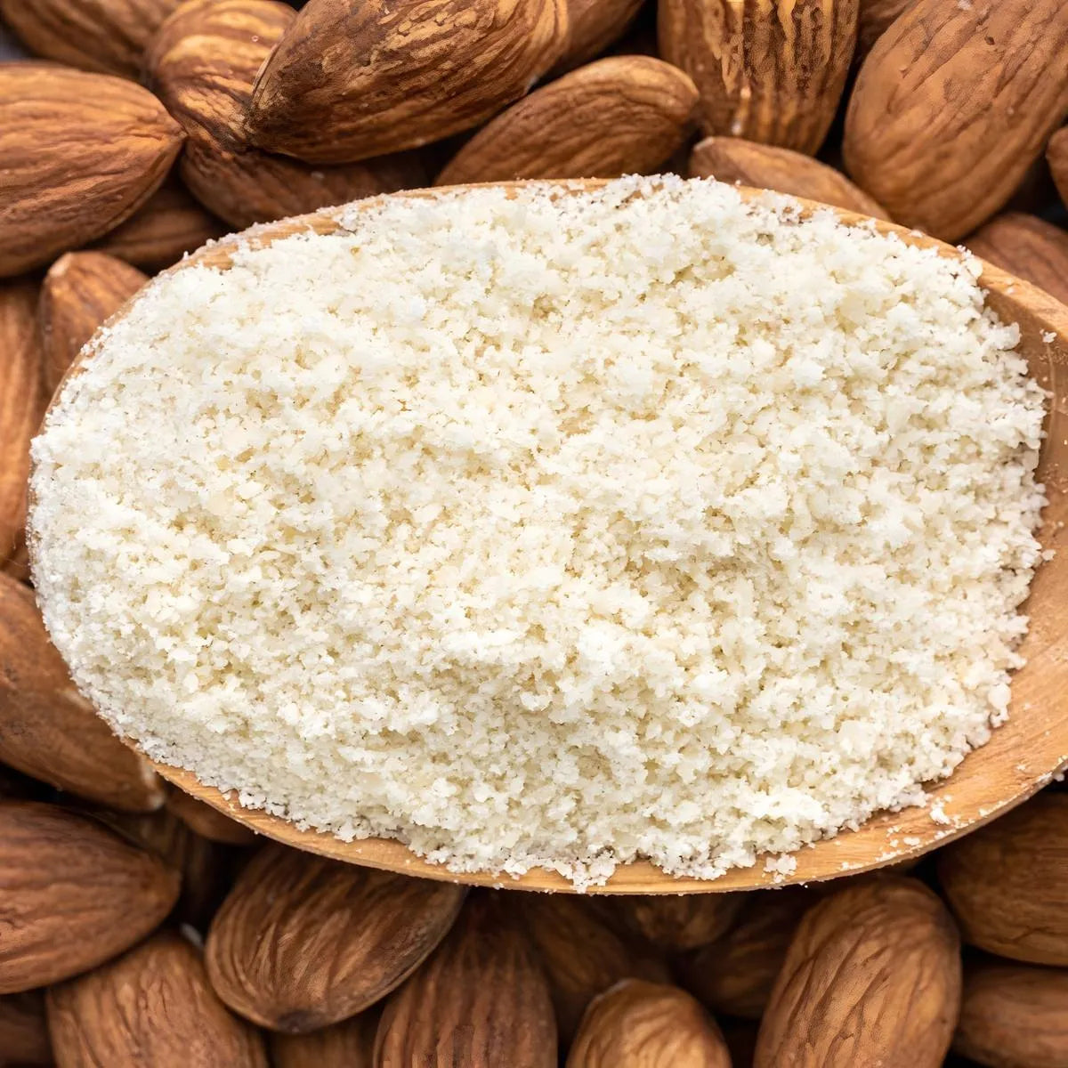Poudre d'amande fine PROFRUIT dans une cuillère en bois sur fond d'amandes entières, parfaite pour recettes sucrées et salées.